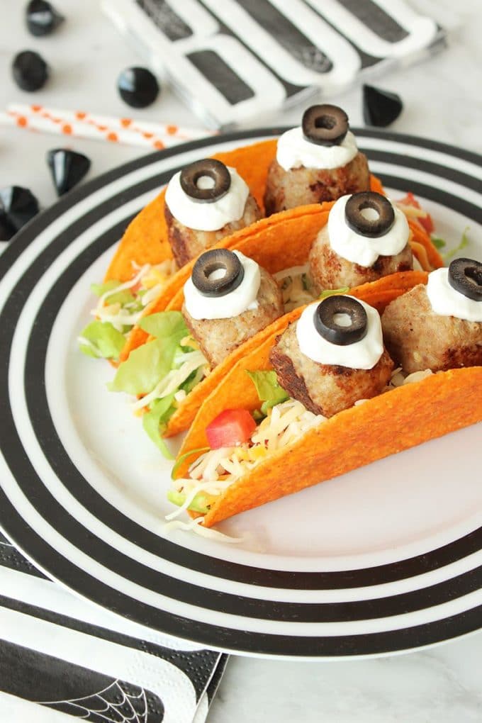 Three Scary Nacho Monster Tacos for Halloween on a plate with meatballs and olive slices ons sour cream for eyes. 