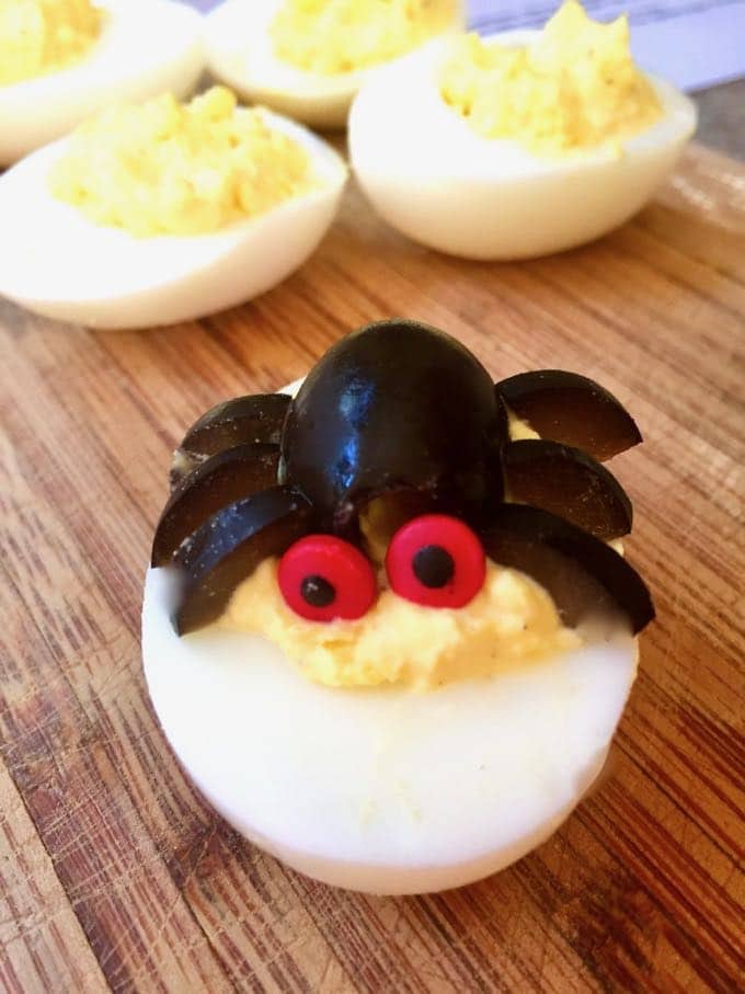Halloween deviled eggs with black olive body and legs and red googly eyes. .