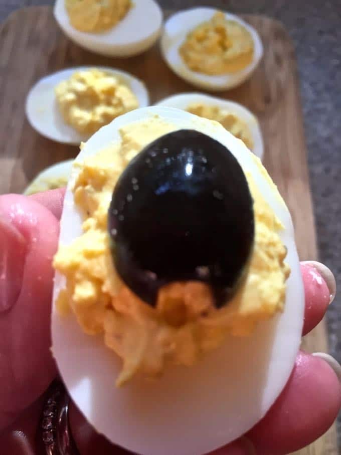 Adding the olive body to Halloween deviled eggs.