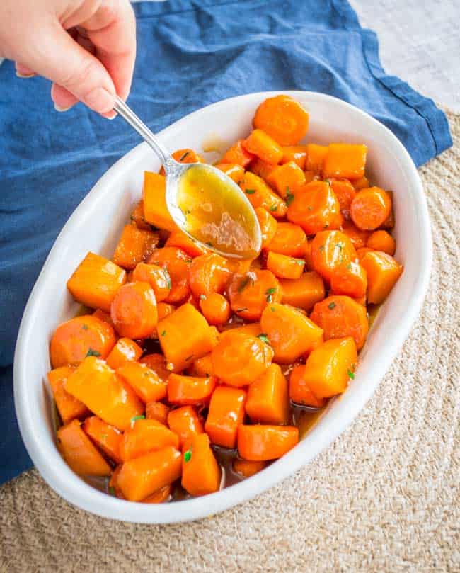 An oval white serving dish full of cooked carrots.