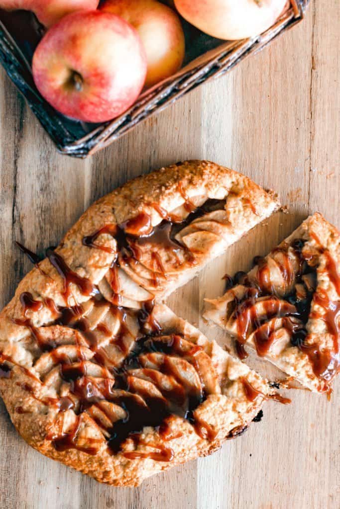 A apple galette topped with caramel with apples in the background.