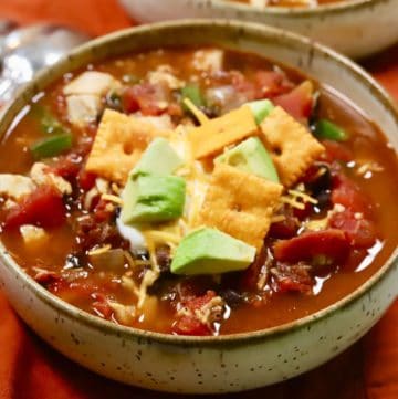 Turkey Chili in a white bowl garnished with sour cream, sliced avocado, and tortilla chip.