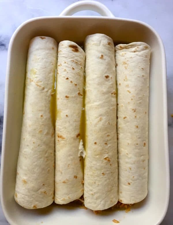 Four rolled tortillas in a white baking dish.