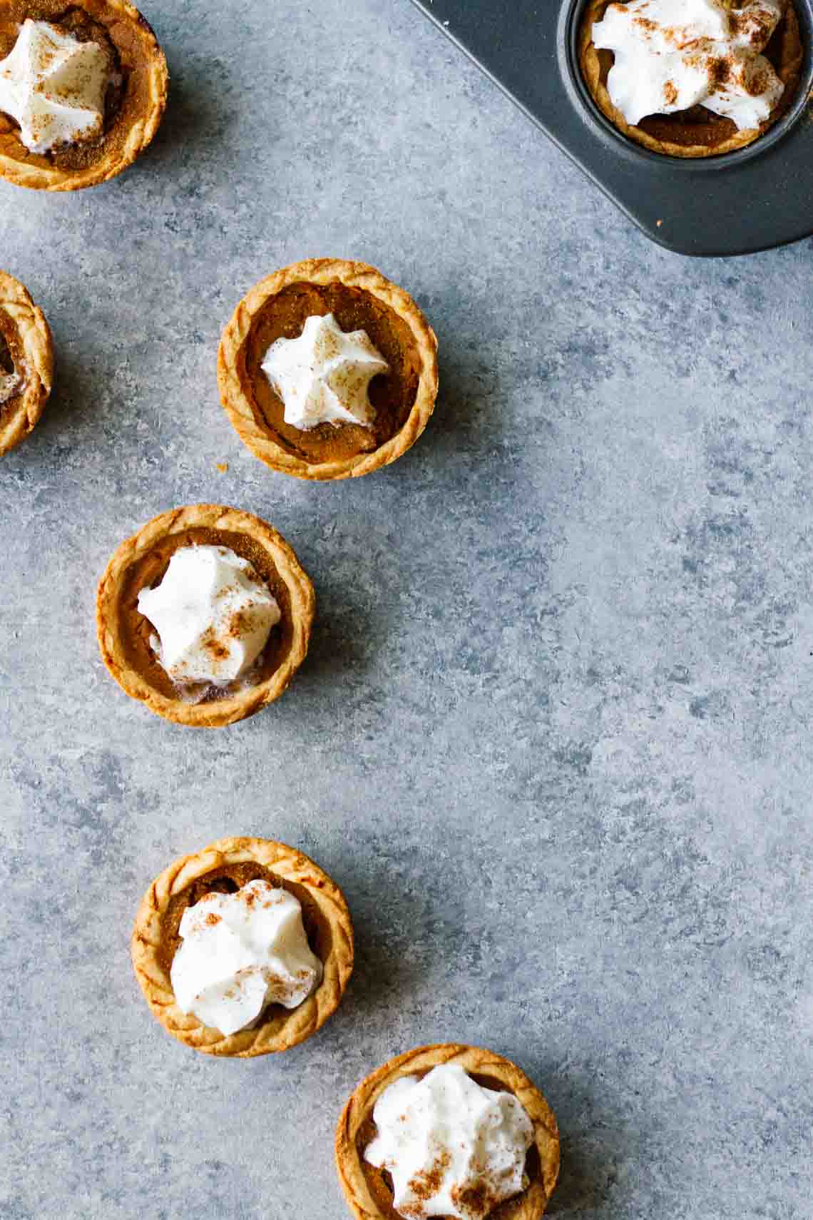 Five mini pumpkin pies topped with whip cream on a counter.