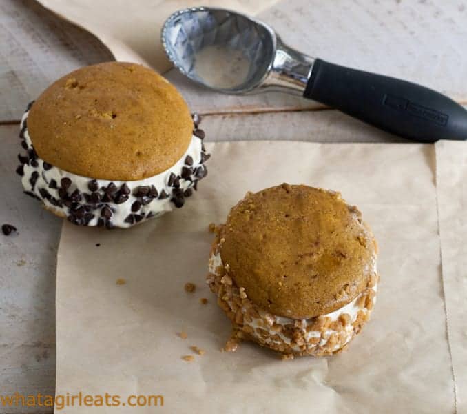 Two pumpkin ice cream sandwiches on a piece of paper with an ice cream scoop in the background.
