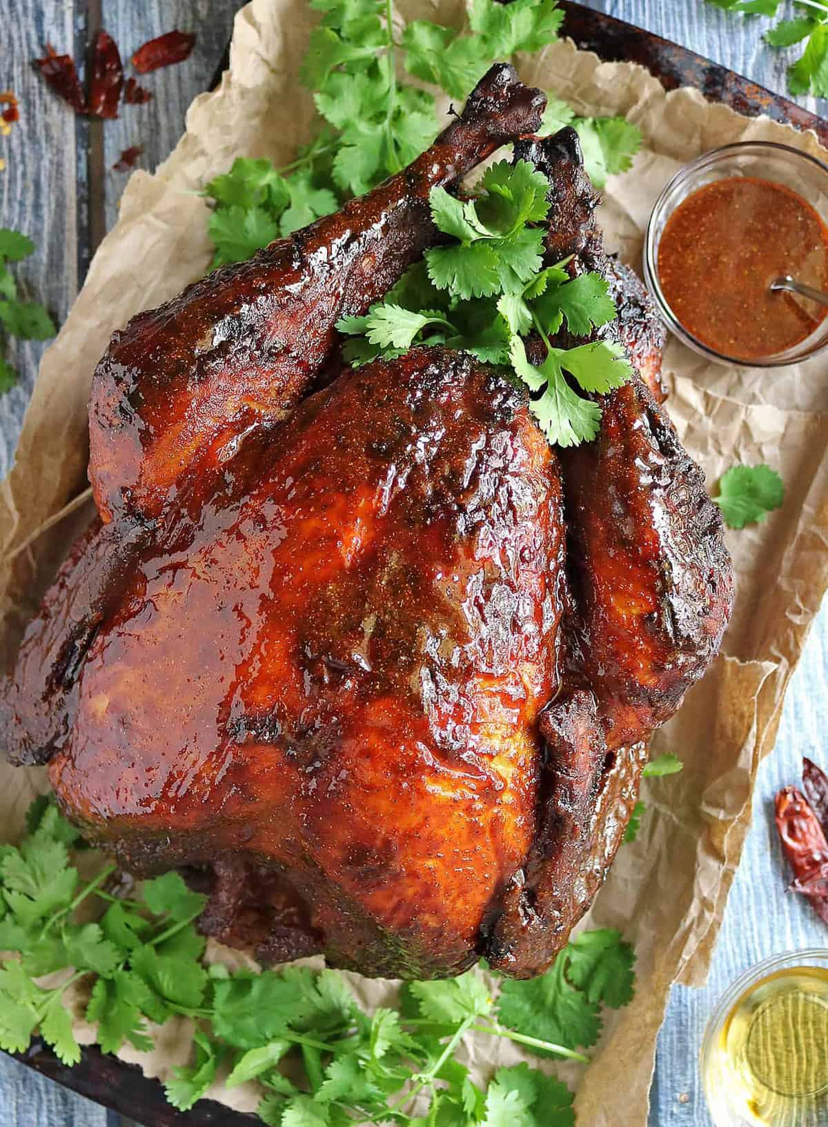 A baking sheet covered with a brown paper bag holding a large honey glazed cooked turkey.