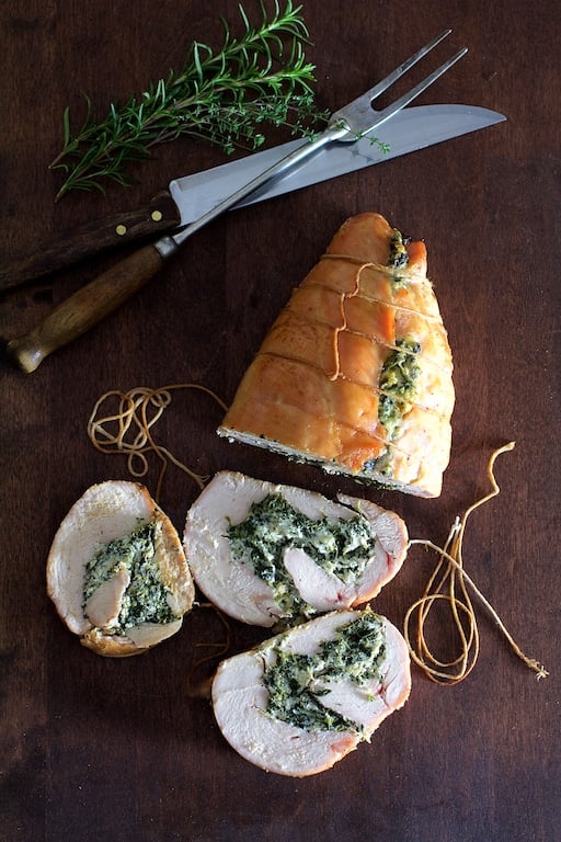 Spinach and Ricotta-Stuffed Turkey Breast with Garlic and Herb Sauce on a cutting board with fresh herbs.