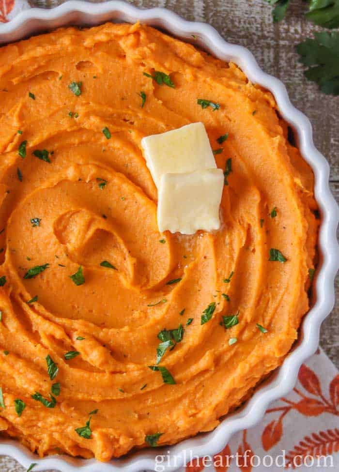 A white dish with whipped sweet potatoes topped with pats of butter.