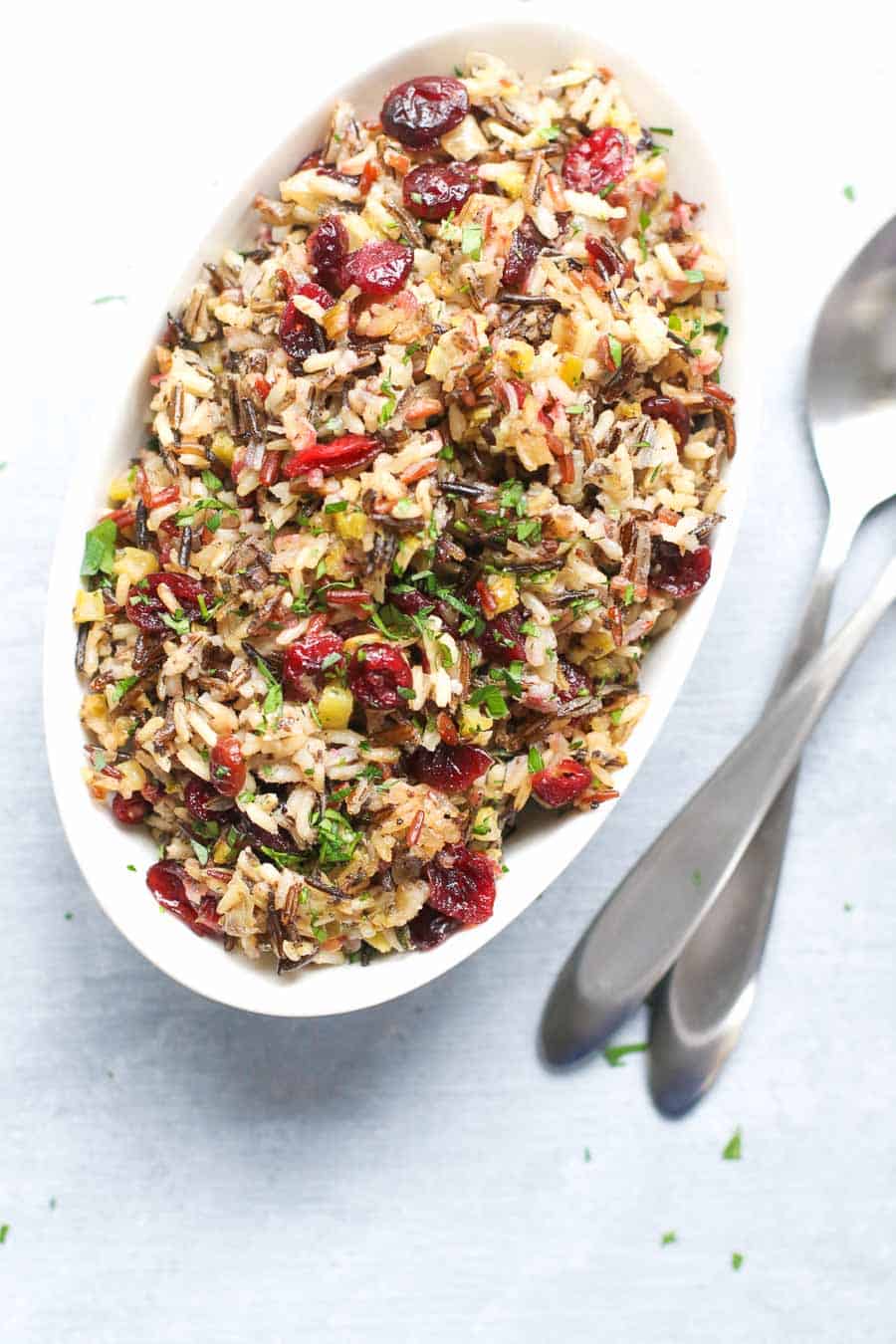 Vegan Wild Rice Stuffing in an oval glass baking dish with serving utensils. 