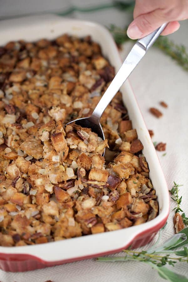 Sausage pecan and pear dressing in a red baking dish with sage leaves next to it. 