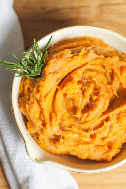 Mashed sweet potatoes with caramelized onions in a bowl with a sprig of rosemary. 