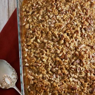 A large baking dish full of sweet potato casserole topped with pecans and brown sugar.