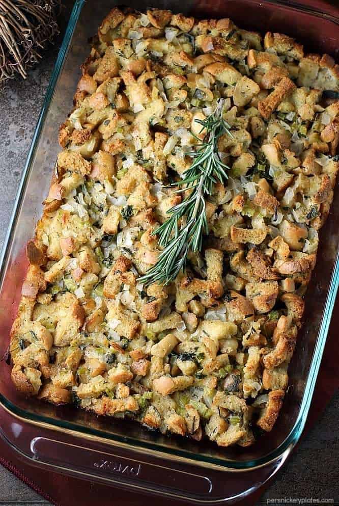 Traditional herb stuffing in a large clear glass baking dish topped with a sprig of rosemary. 