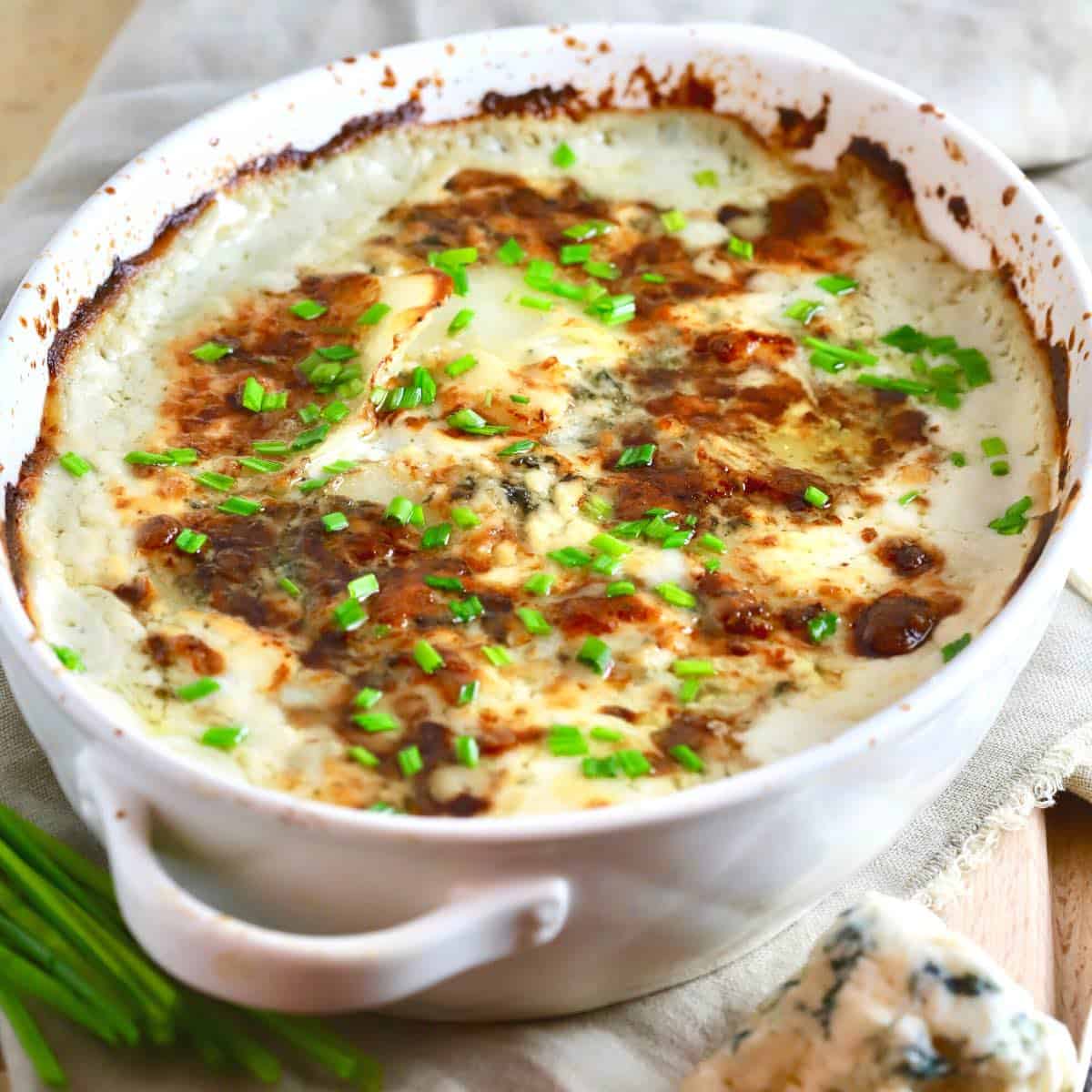 A white casserole dish of Cheese Potatoes Au Gratin on the Thanksgiving table.