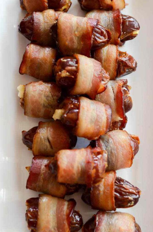 Bacon wrapped stuffed dates on a white serving platter. 