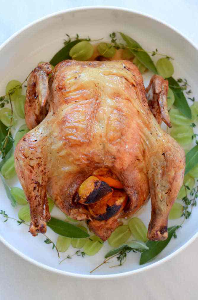 Roasted Chicken on a plate garnished with grapes and sage leaves. 