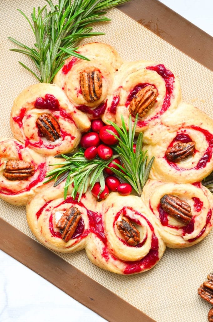 A wreath made out of crescent rolls, cranberries and brie cheese garnished with rosemary. 