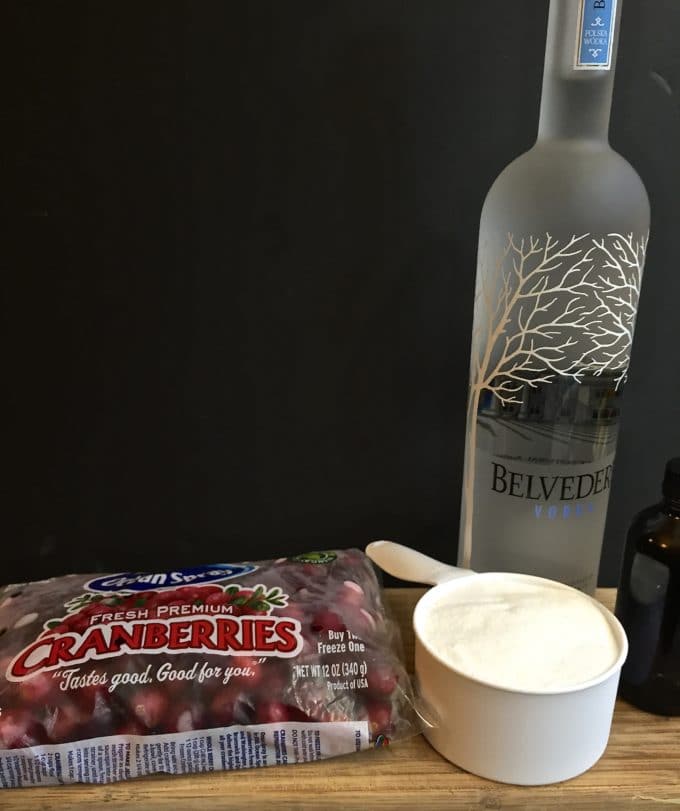 A bottle of vodka, cranberries, sugar and vanilla on a cutting board. 