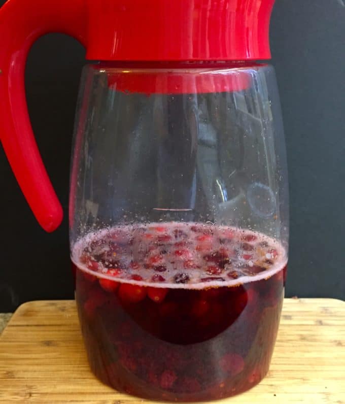 Vodka with cranberries in a plastic pitcher on a wooden cutting board. 