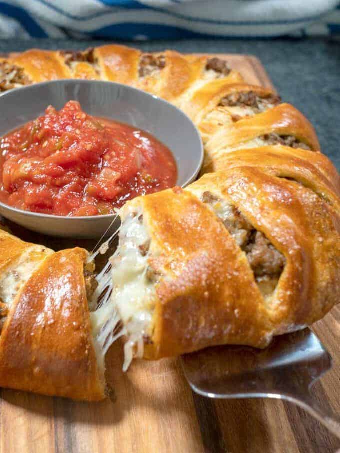 Sausage crescent roll ring full of cheese and sausage with a dip in the middle. 