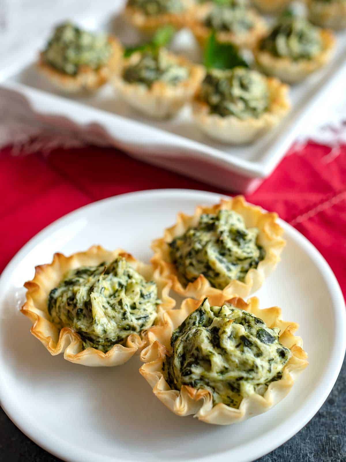 Three spinach artichoke tartlets on a white plate. 