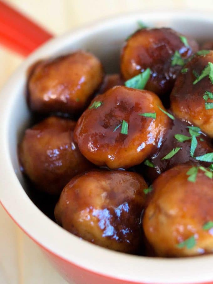 A white bowl full of meatballs garnished with parsley. 