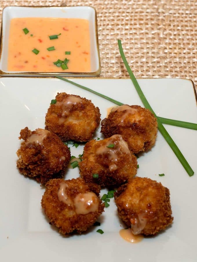 Six pieces of Bang Bang Chicken on a square white plate, garnished with chives.