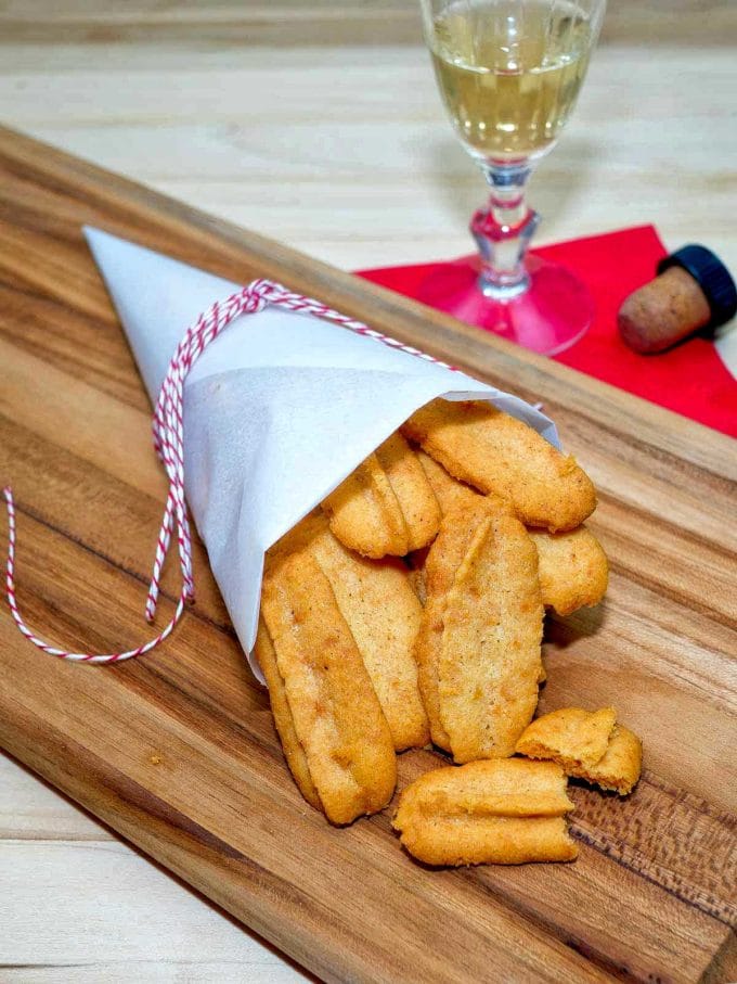 Southern Cheese Straws wrapped in a paper cone on a wooden cutting board.