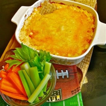 Buffalo Chicken Dip in a small baking dish with celery, carrots, and triscuits on the side.