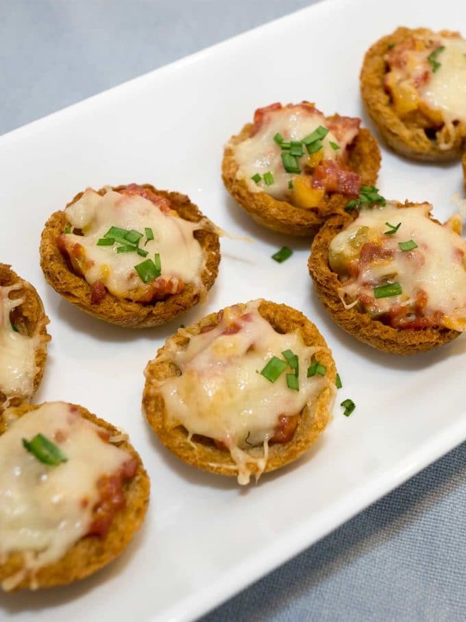 Mini Reuben Croustades topped with cheese and parsley on a white serving plate.