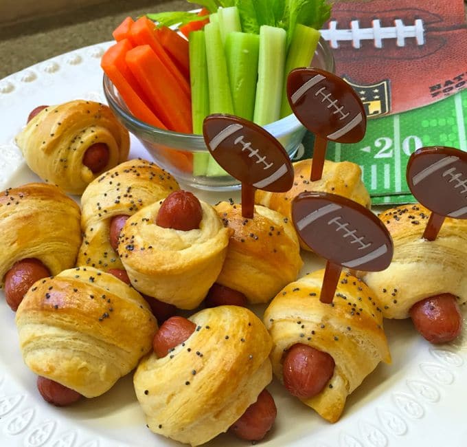 Pigs in a Blanket topped with poppy seeds with plastic football shaped picks.