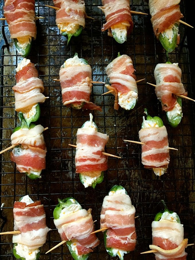 Peppers stuffed with cheese and wrapped with bacon on a wire rack over a baking sheet ready for the oven. 