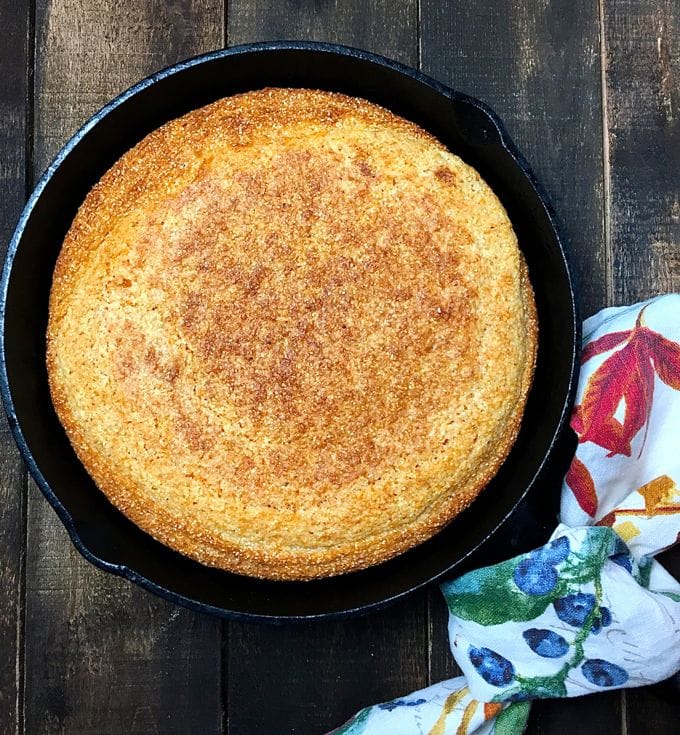 Baked cornbread in a cast iron skillet on a wooden cutting board. 