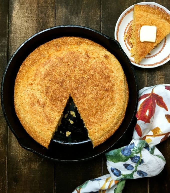 Cornbread in a cast-iron skillet with a slice on a small plate. 