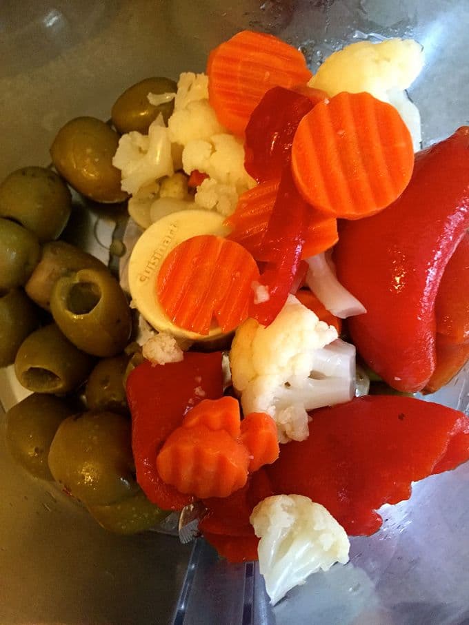 Using a food processor to cut olives, carrots, cauliflower and red bell pepper.