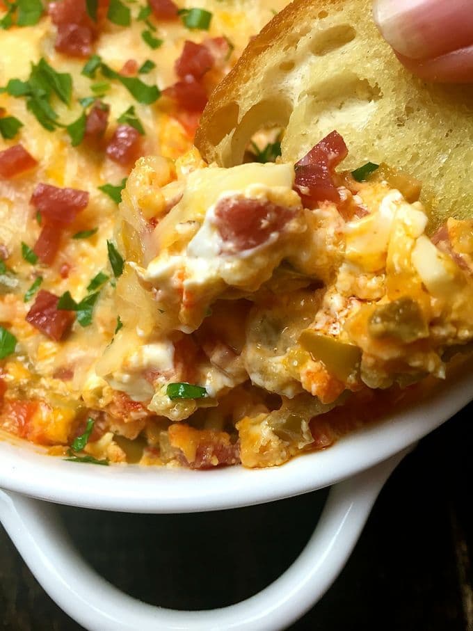 Easy Mardi Gras Hot Muffuletta Dip in a white bowl with toasted bread rounds.