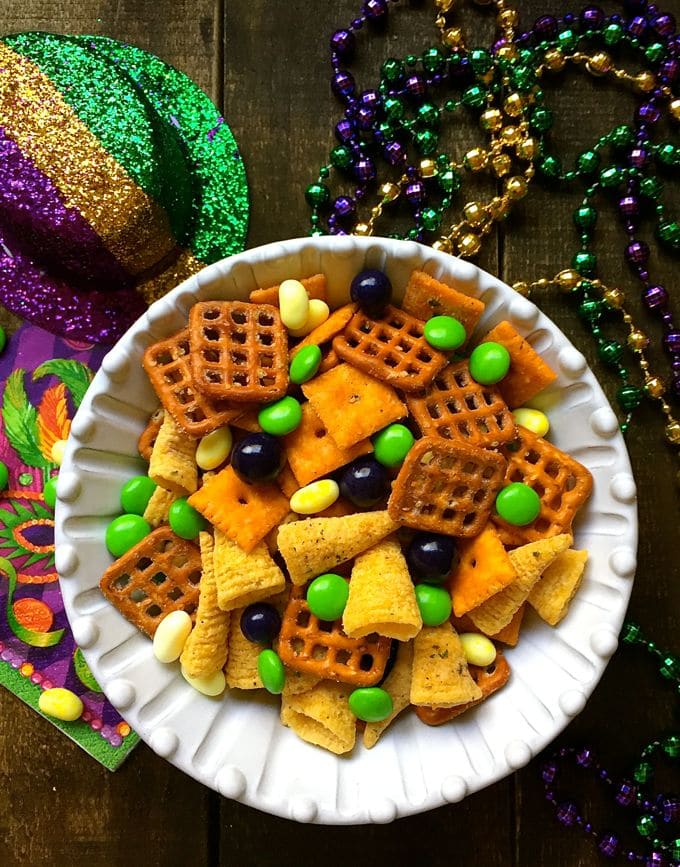 A white bowl with mardi gras snack mix and green, gold and purple candy. 