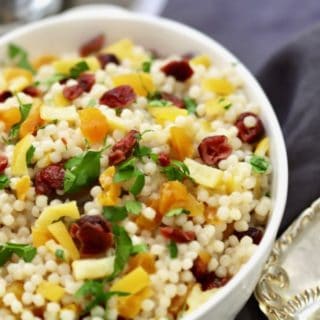 Pearl Couscous with Preserved Lemon in a bowl with cranberries, apricots, parsley, and pistachios in a white serving bowl