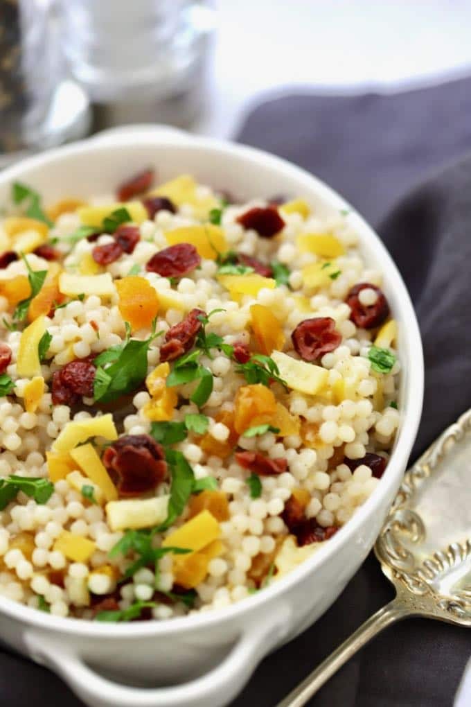 Pearl Couscous with Preserved Lemon in a bowl with cranberries, apricots, parsley, and pistachios in a white serving bowl