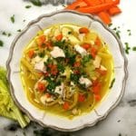 Roasted Chicken Noodle Soup garnished with parsley in a white bowl with carrots and celery on the outside.