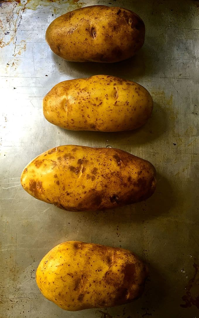 Four baked potatoes on a baking sheet.