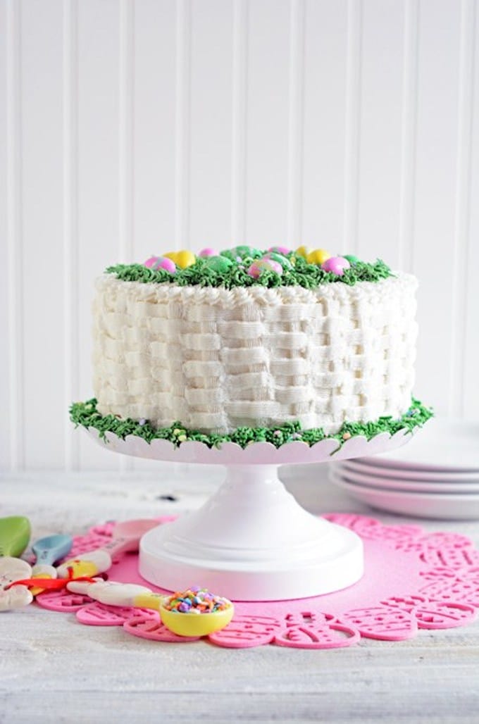 A beautiful cake with white icing piped in a basket weave pattern topped with candy Easter eggs. 