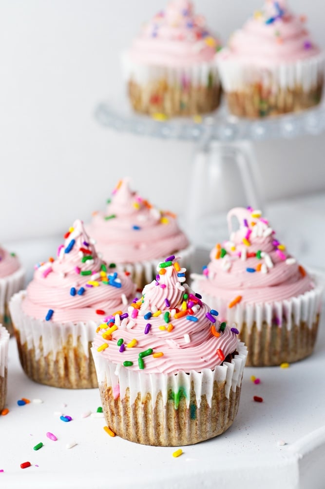 Cupcakes topped with pink icing and multicolor sprinkles. 