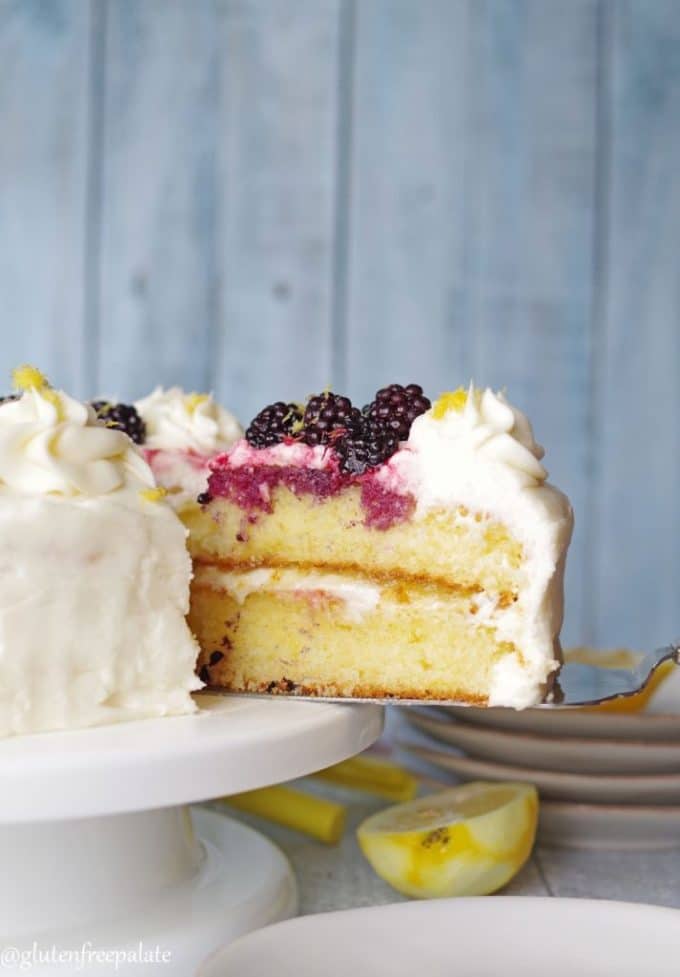 A slice of white cake topped with white icing and blackberrries. 