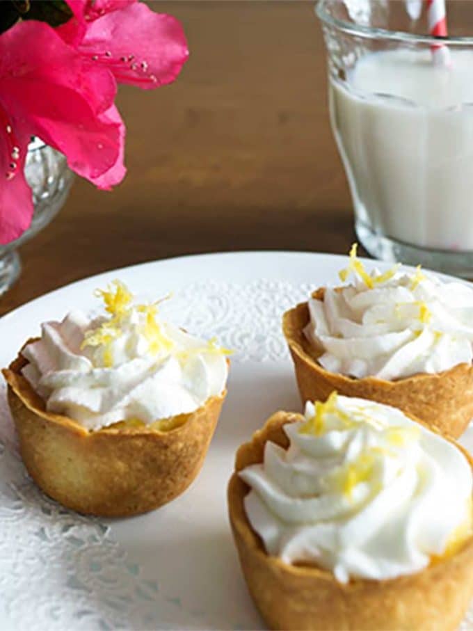 Three tartlets with lemon filling topped with whipped cream and lemon zest. 