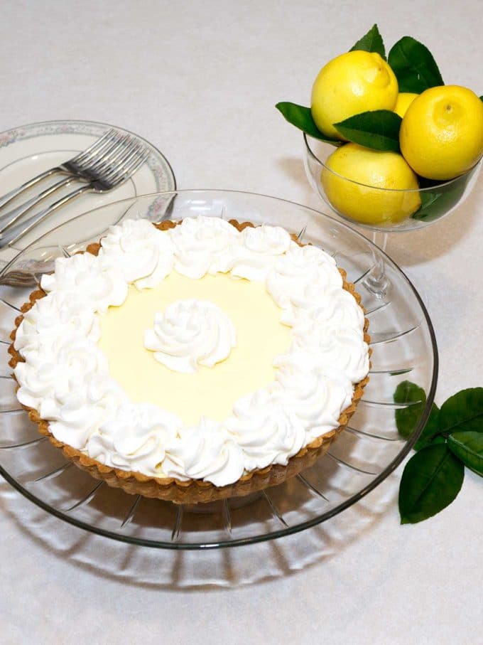 A french cream tart on a clear glass plate topped with whipped cream. 