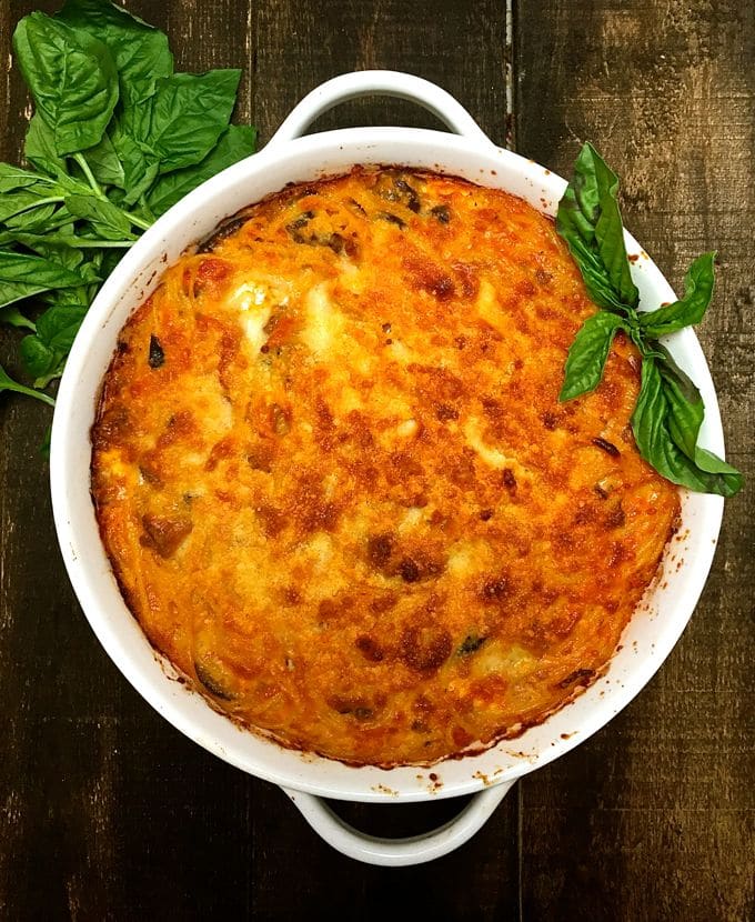 A white baking dish full of Easy Baked Spaghetti Pie and garnished with fresh basil ready to serve