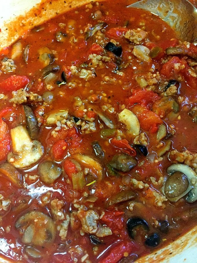 A photo of tomato sauce being added to a skillet with mushrooms and sausage for Easy Baked Spaghetti Pie Casserole