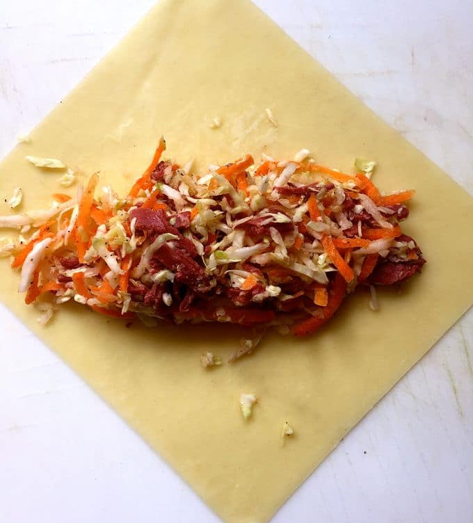 A spoonful of cabbage and corned beef in the center of an egg roll wrapper. 