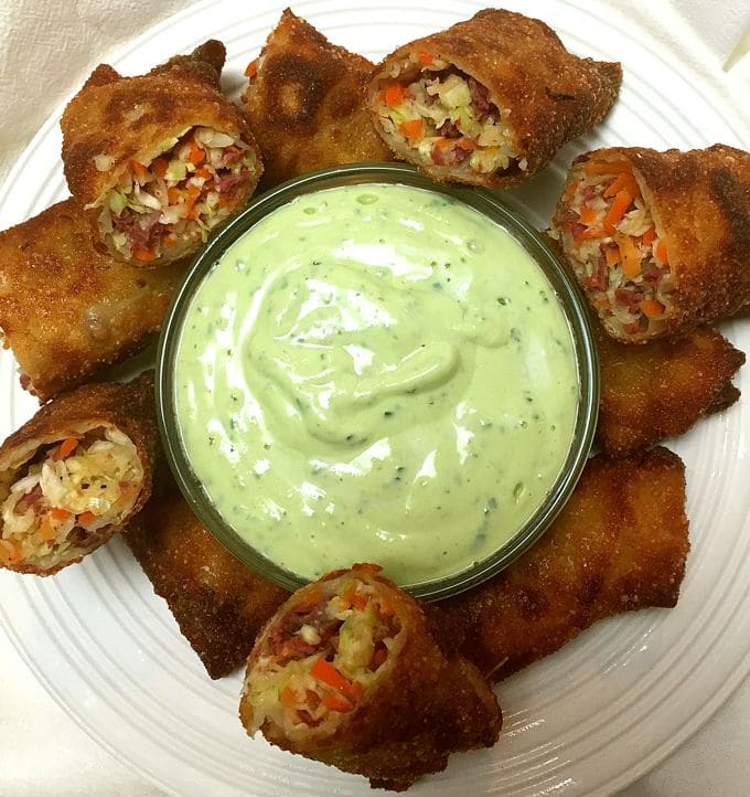 Corned-Beef-and-Cabbage-Egg-Rolls cut in half on a plate with Avocado Lime Dressing